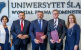 Pięć osób pozuje do zdjęcia na tle napisu „Uniwersytet Śląski, Wydział Prawa i Administracji”. Dwie osoby trzymają bordowe teczki konferencyjne.