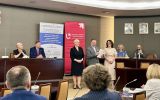 Osoby prowadzące konferencję stoją i siedzą przy stole prezydialnym w sali obrad. W tle widoczne są roll-upy XXV Jubileuszowej Konferencji Naukowej SEAP oraz Wydziału Prawa i Administracji Uniwersytetu Łódzkiego.