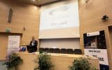 Prelegent stoi przy mównicy w auli Uniwersytetu Rzeszowskiego, a na ekranie wyświetlona jest prezentacja NATO Stability Policing Centre of Excellence.