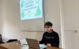 Prelegent siedzi przy laptopie pod ekranem projekcyjnym. Na slajdzie widoczny jest tytuł prezentacji o estońskim CIT jako instrumencie wsparcia sektora MŚP.