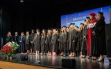 Grupa absolwentek pozuje na scenie wraz z przedstawicielami władz uczelni.