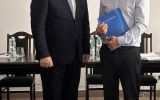 Dwóch mężczyzn pozuje w sali posiedzeń; jeden trzyma granatową teczkę z logo Uniwersytetu Rzeszowskiego.