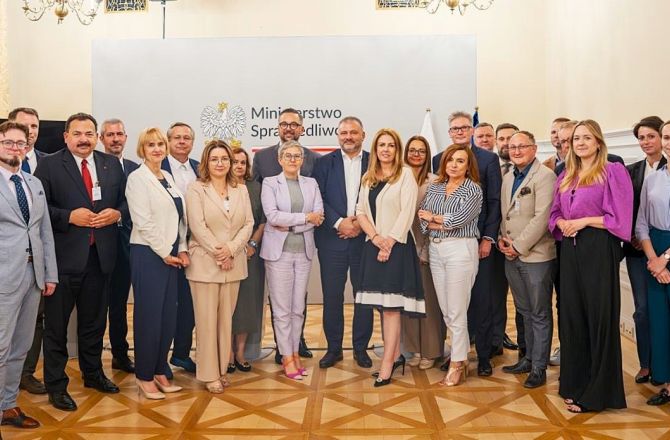 Uczestnicy spotkania stoją do wspólnego zdjęcia grupowego na tle baneru Ministerstwa Sprawiedliwości.