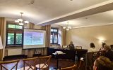 Prelegentka przedstawia referat dotyczący dostępności administracji w urzędach miejskich miast wojewódzkich dla osób ze szczególnymi potrzebami. Obok widoczny jest ekran z prezentacją oraz uczestnicy seminarium.