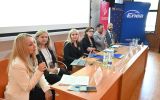 Panelistki i paneliści siedzą przy stole podczas dyskusji, w tle widoczne banery partnerów wydarzenia.