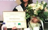 Laureatka w todze i birecie pozuje z dyplomem Doctor Honoris Causa oraz bukietem.