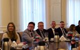 Grupa uczestników spotkania siedzi przy stole konferencyjnym w eleganckiej sali urzędowej.
