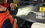 Uczestnik Pikniku Nauki obserwuje ślady daktyloskopijne oświetlane specjalistyczną lampą na stanowisku kryminalistycznym WPA