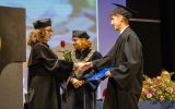 Absolwent odbiera dyplom i uścisk dłoni od przedstawicielki władz uczelni podczas ceremonii.