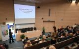 Prezentacja w audytorium podczas UR AI Summit. Na ekranie widoczny jest slajd „Od króla polskiego nieba do polskiej sztucznej inteligencji”, a uczestnicy siedzą na widowni.