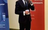 Prelegent wygłasza wystąpienie podczas II Forum Cooperante, stojąc obok banerów organizatorów.
