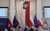 Uczestnicy debaty „Europa jest kobietą!” siedzą na scenie w sali Podkarpackiego Urzędu Wojewódzkiego, na tle flag Polski i Unii Europejskiej.