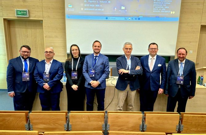 Grupa uczestników UR AI Summit pozuje do zdjęcia w sali konferencyjnej przed ekranem projekcyjnym.