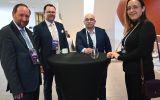 Cztery osoby z identyfikatorami UR AI Summit stoją przy wysokim stoliku.