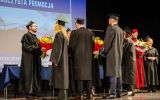 Absolwenci wręczają bukiety kwiatów przedstawicielom władz uczelni na zakończenie uroczystości.