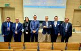 Grupa uczestników UR AI Summit pozuje do zdjęcia w sali konferencyjnej przed ekranem projekcyjnym.