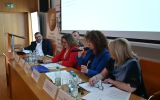Panelistki i paneliści siedzą przy stole prezydialnym podczas dyskusji konferencyjnej.