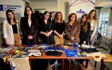 Grupa osób stoi przy stoisku Uniwersyteckiej Poradni Prawnej i ELSA Rzeszów. Na stole znajdują się materiały promocyjne i gadżety edukacyjne.