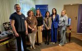 Grupa organizatorów stoi przy stanowisku z materiałami kryminalistycznymi i sprzętem edukacyjnym. W tle widoczne są roll-upy instytucji partnerskich.