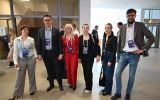 Grupa uczestników konferencji pozuje do zdjęcia w holu budynku. Osoby mają identyfikatory konferencyjne.
