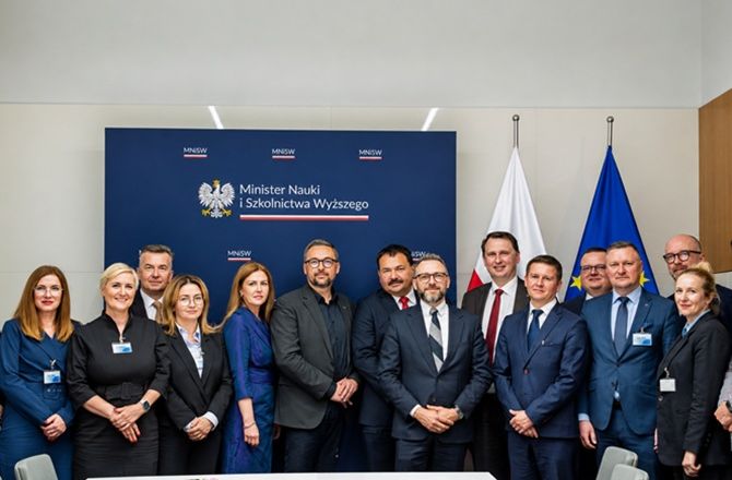 Uczestnicy spotkania pozują w sali Ministerstwa Nauki i Szkolnictwa Wyższego na tle baneru z oznaczeniem MNiSW oraz flag Polski i Unii Europejskiej.
