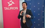 Uczestnik konferencji wygłasza wystąpienie z mikrofonem na tle banerów Uniwersytetu Rzeszowskiego i TAURON.