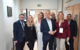 Grupa uczestników konferencji pozuje do zdjęcia w korytarzu przy wejściu do sali obrad.