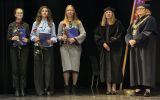 Trzy studentki trzymające teczki i róże pozują do zdjęcia z dwiema przedstawicielkami wydziału w strojach akademickich.