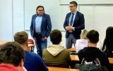 Dwóch prowadzących stoi przed studentami w sali dydaktycznej i zwraca się do uczestników spotkania.