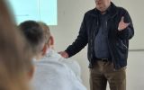 Spotkanie w sali wykładowej z udziałem prelegenta stojącego przed tablicą.