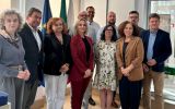 Grupa jedenastu osób pozuje do wspólnej fotografii w jasnym wnętrzu instytucji. W tle widoczne są flagi, w tym flaga Unii Europejskiej i Portugalii.