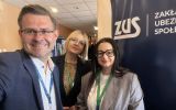 Trzy osoby uczestniczące w konferencji pozują do pamiątkowego zdjęcia na tle baneru Zakładu Ubezpieczeń Społecznych.