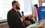 Prelegent z mikrofonem występuje przy mównicy podczas sesji otwierającej konferencję.