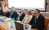 Uczestnik panelu zabiera głos z mikrofonem przy stole prezydialnym.