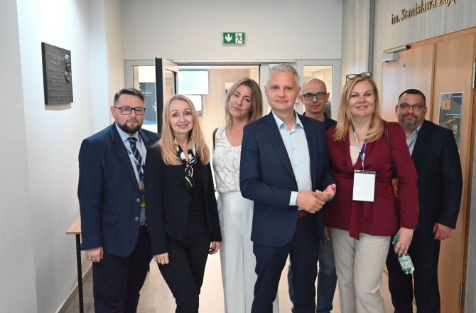 Grupa uczestników konferencji pozuje do zdjęcia w korytarzu przy wejściu do sali obrad.