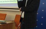 Prelegent przemawia z mikrofonem na tle ścianki Wydziału Prawa i Administracji UR.
