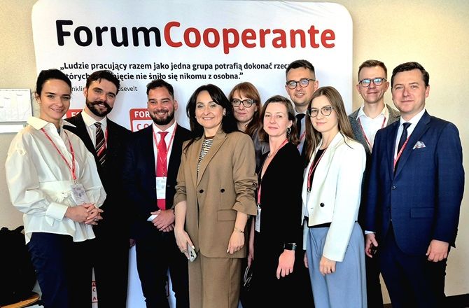 Uczestnicy II Forum Cooperante pozują do wspólnego zdjęcia przy ściance z logo wydarzenia.