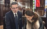 Uczestniczka wizyty akademickiej podpisuje dokument przy stole w reprezentacyjnej sali instytucji prawniczej; obok stoi mężczyzna wskazujący miejsce podpisu.