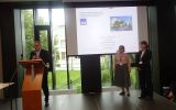 Konferencja z udziałem prelegenta za mównicą oraz dwóch kobiet stojących na scenie.
