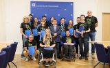 Grupa studentów oraz przedstawicieli Uniwersytetu Rzeszowskiego podczas uroczystości wyróżnienia za sukcesy sportowe. W środku stoi rektor UR.