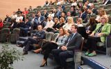 Uczestnicy konferencji siedzący w rzędach w audytorium. Na pierwszym planie widoczne są osoby słuchające wystąpienia.