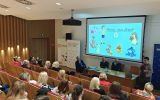 Prelegentka występuje przed uczestnikami; na ekranie widoczny jest slajd „Poznaj nasz zespół”.