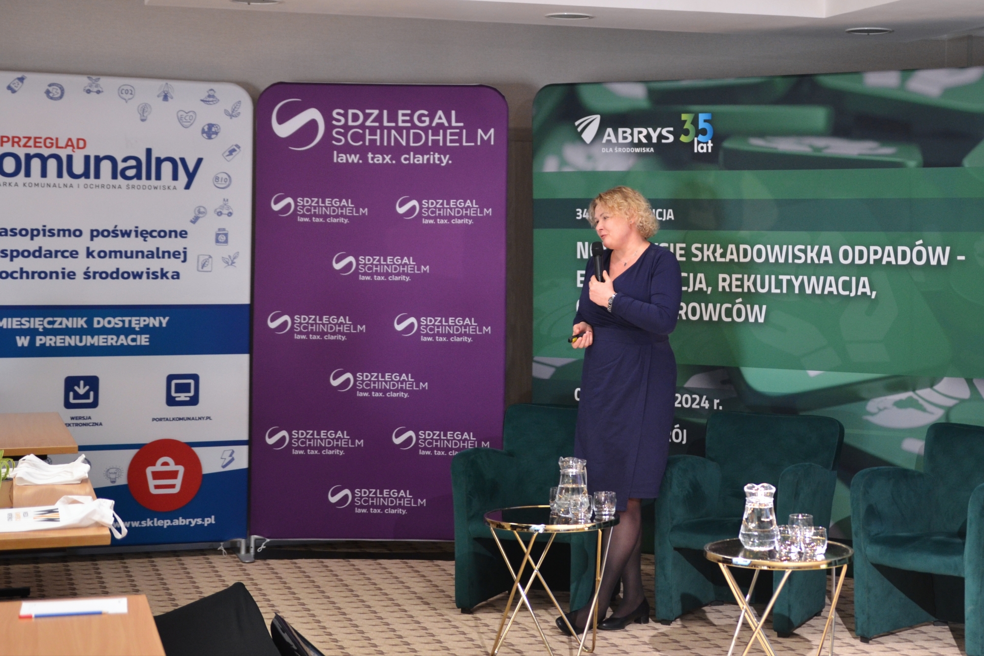 Prof. Justyna Jurczyk stoi przed banerami konferencji ze wskaźnikiem w ręku