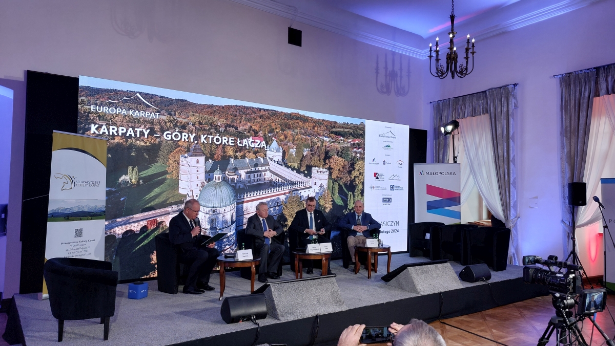 Prelegenci siedzą na scenie, w tle prezentacja - widok zamku