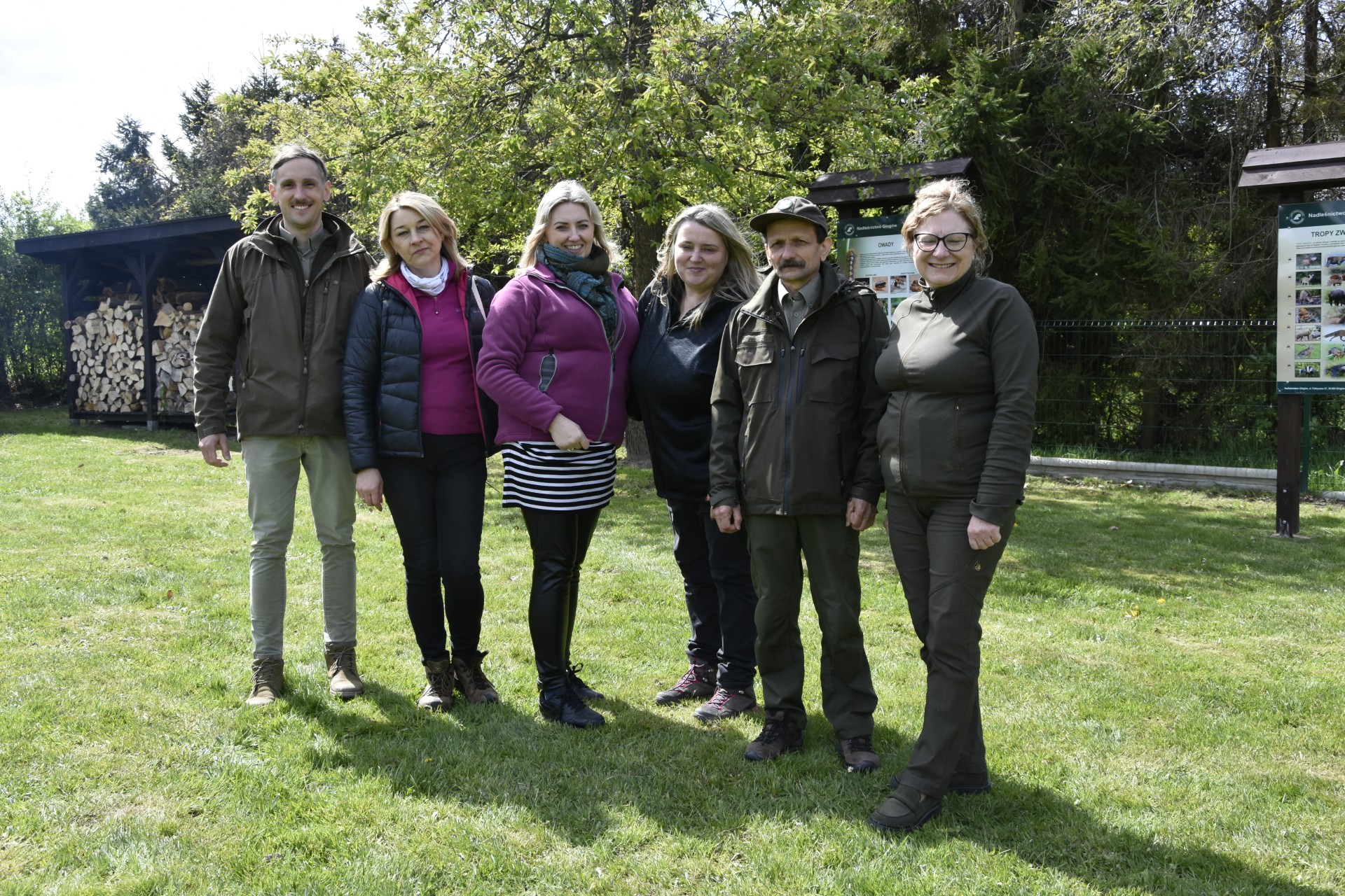 Pracownicy UR pozują do zdjęcia wraz z pracownikami lasów, w tle drzewa i wiata z drewnem