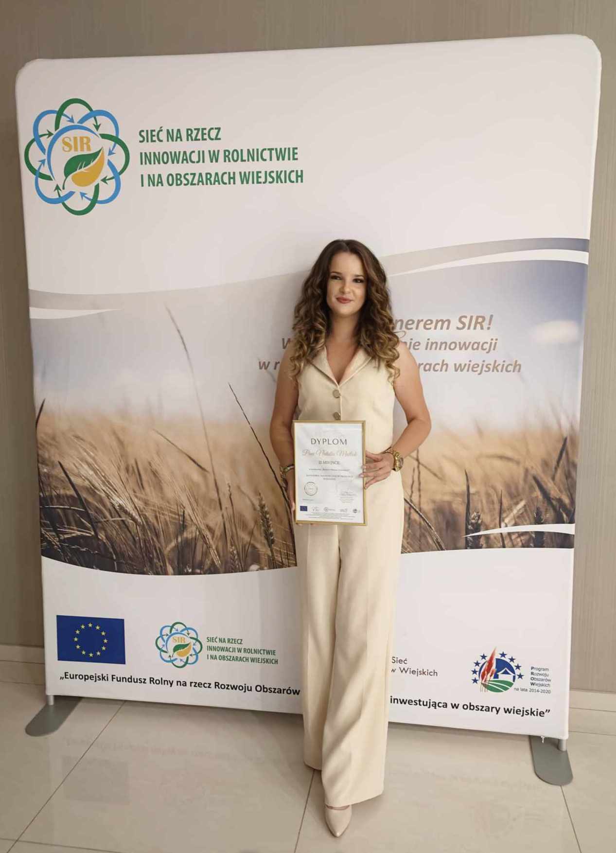 prof Matłok stoi przed banerem przedstawiającym zboże, w ręku trzyma dyplom