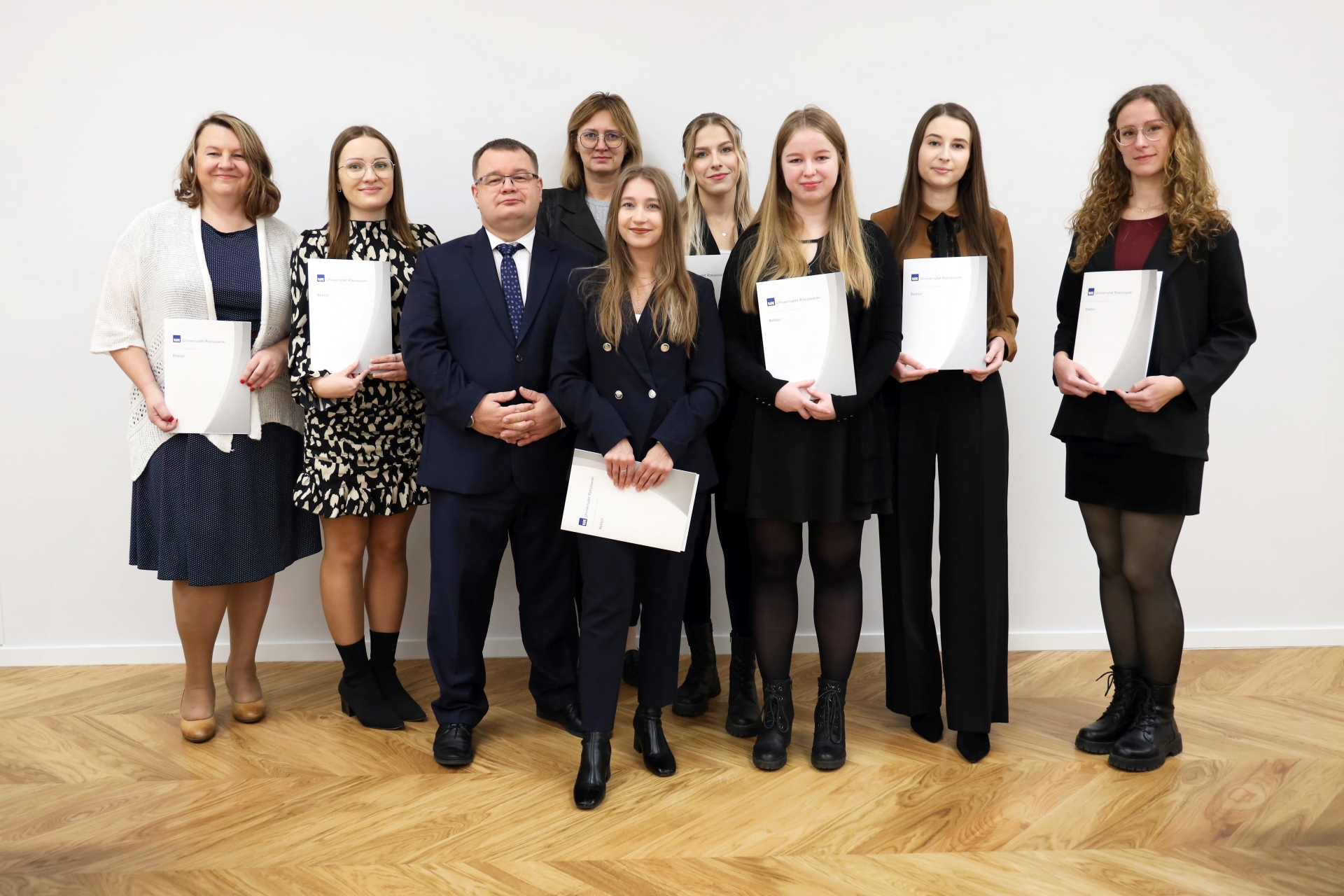 Rektor UR stoi  z nagrodzonymi studentkami, każda z nich trzyma w ręku dyplom