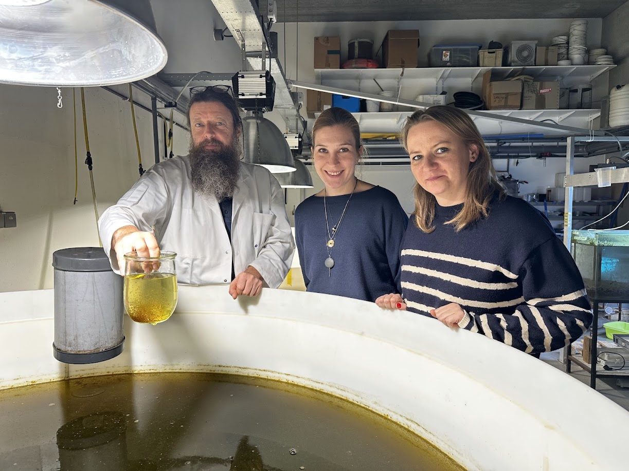 Dr podolak wraz z dwoma innymi osobami pochylona nad zbiornikiem z brązowa cieczą