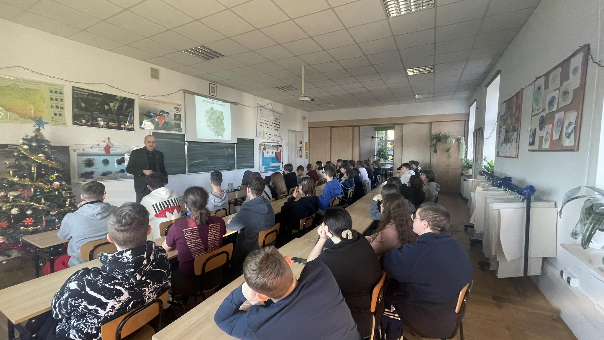 uczniowie siedzą w ławkach, profesor Dudek wygłasza wykład z prezentacją multimedialną