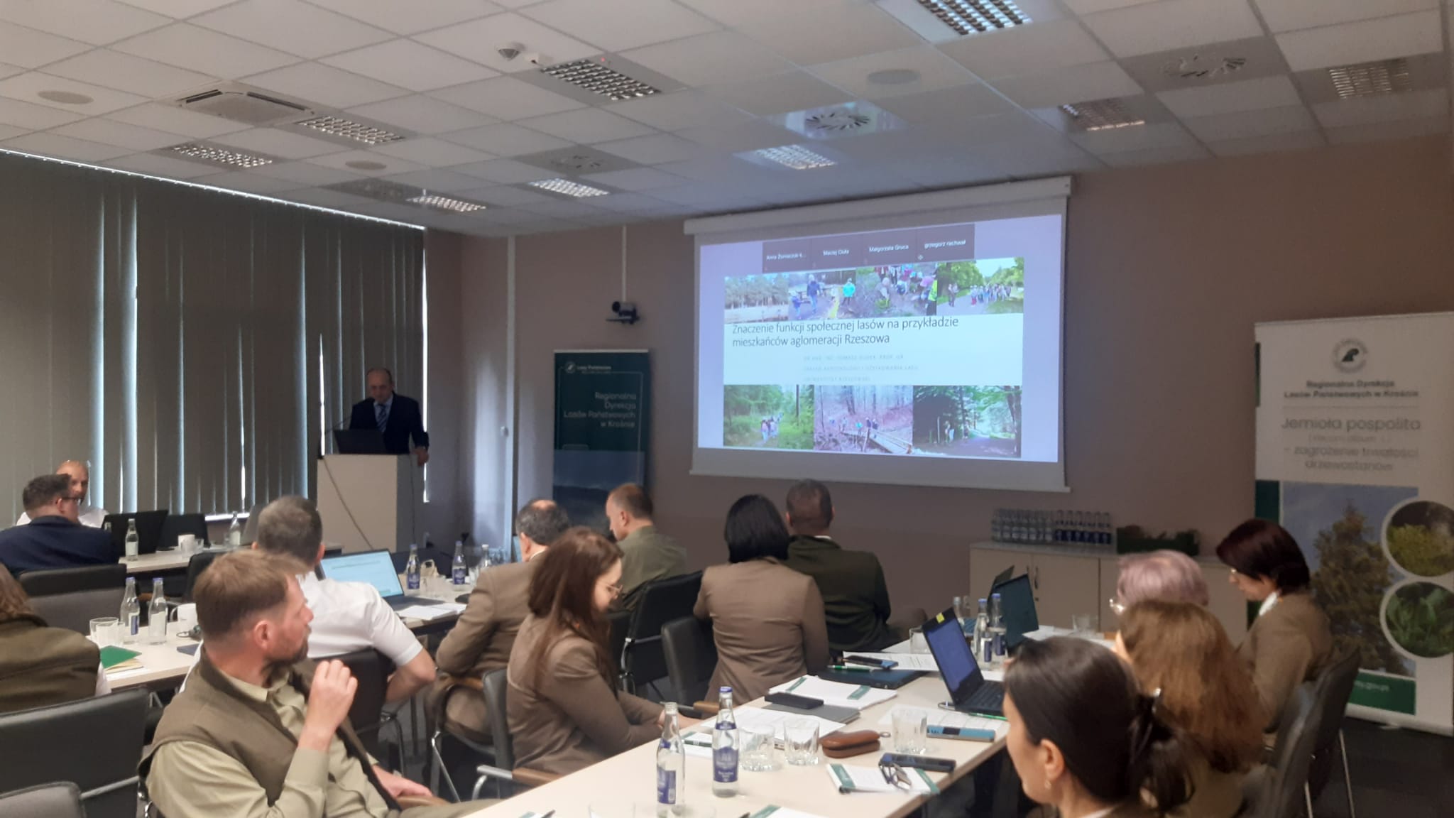 Uczestnicy spotkania w dużej sali siedzą przy stole